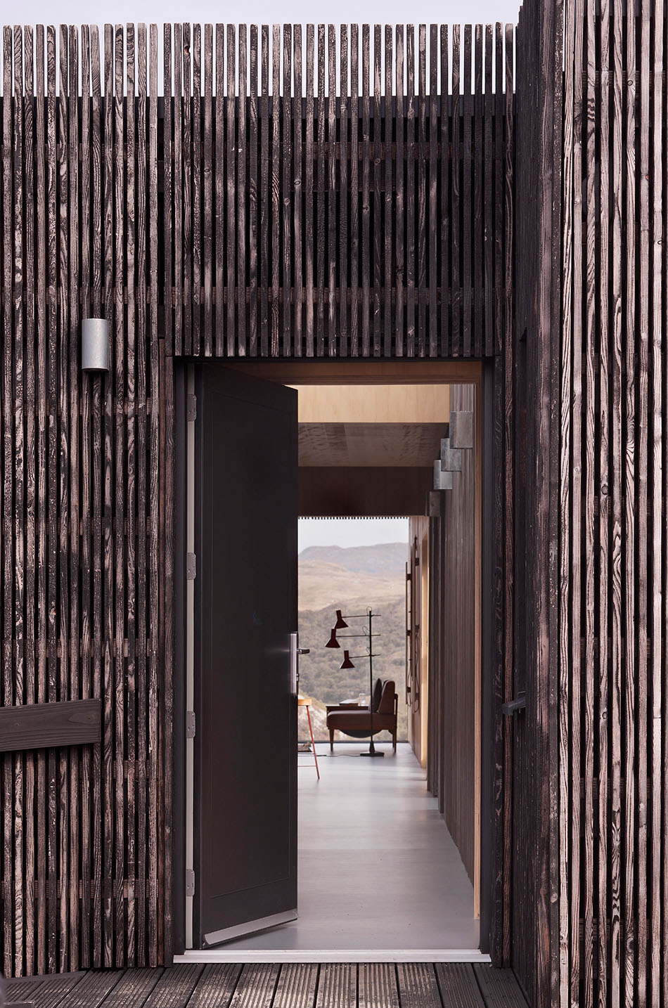 The entryway to An Cala House from the exterior. Larch cladding is seen around the door and the landscape scenery is seen directly as you enter the building.