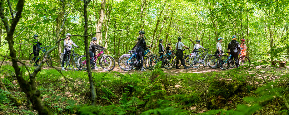 Young people cycling through the woods with Sustains Scotland during the And She Cycles campaign.