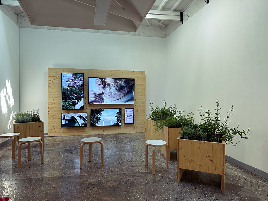 Tv screens, stools and planters in an internal space at the 18th La Biennale di Venezia.