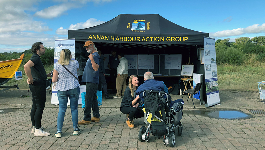 People talking in front of a stand for the Annan Harbour Action Group.