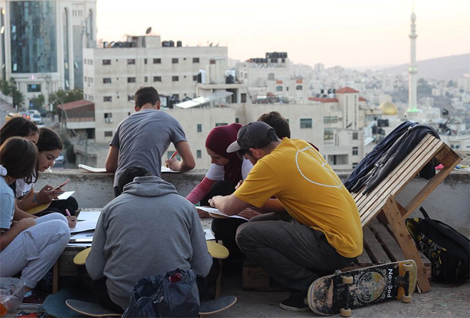 People sat around a table with skateboards on rooftop in Palestine.