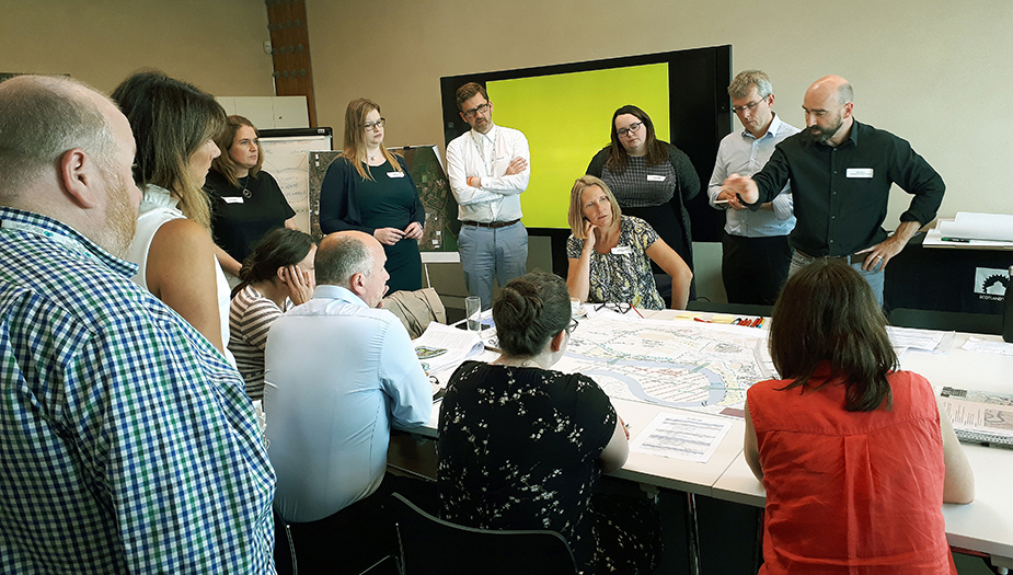 A group of people standing over a table discussing a map during an Architecture and Design Scotland workshop.