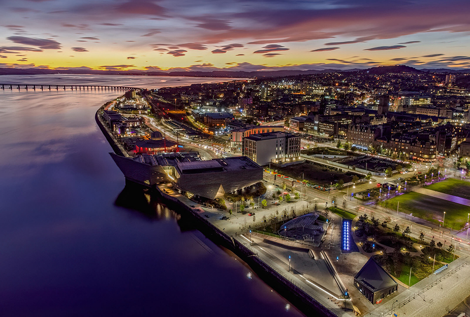 An aerial view of Dundee City at night with the sea and a bridge in the background