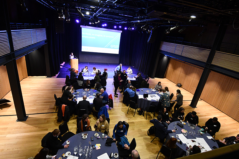 Large hall with round tables filled with people having discussions at the Town Centre Living and Investment Roadshow