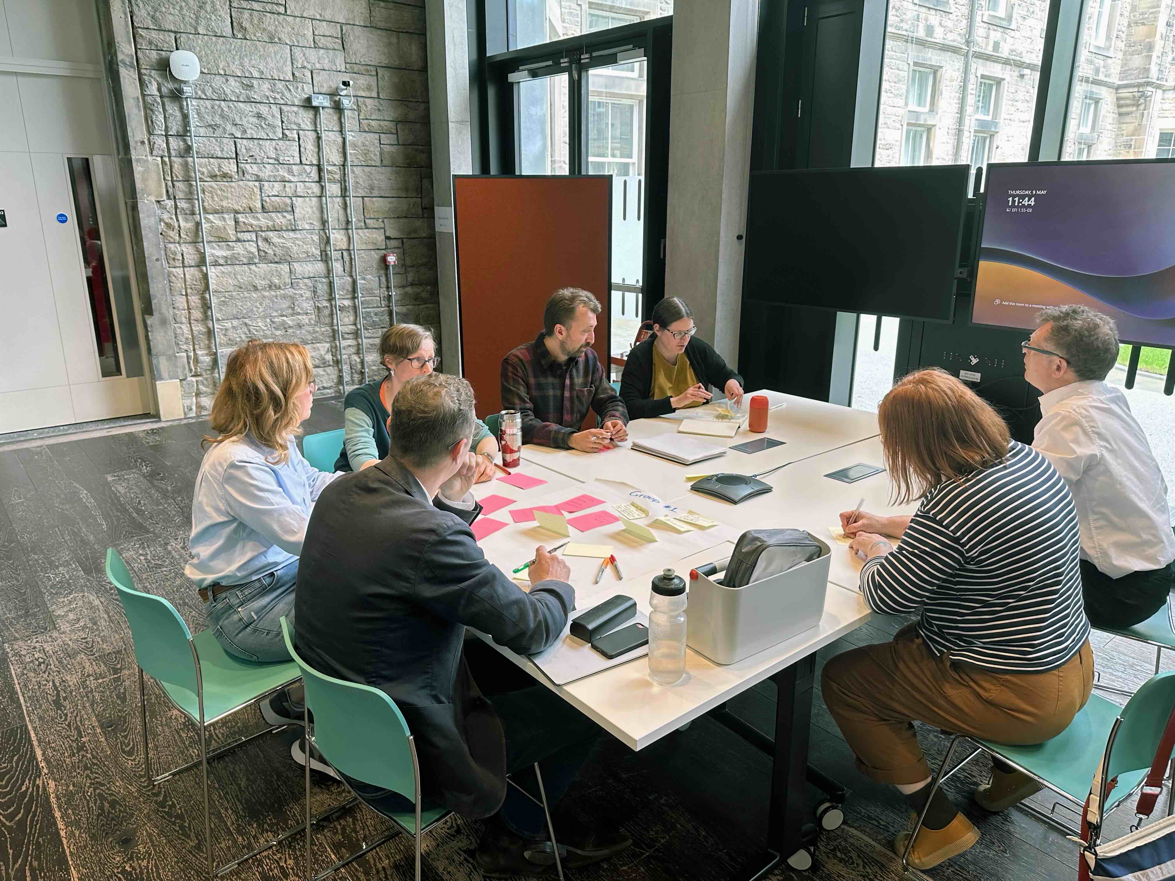 A group of people sit around a white table with multi coloured notes and pens