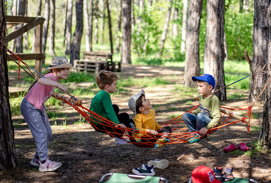 Children playing on a hammock in the woods.