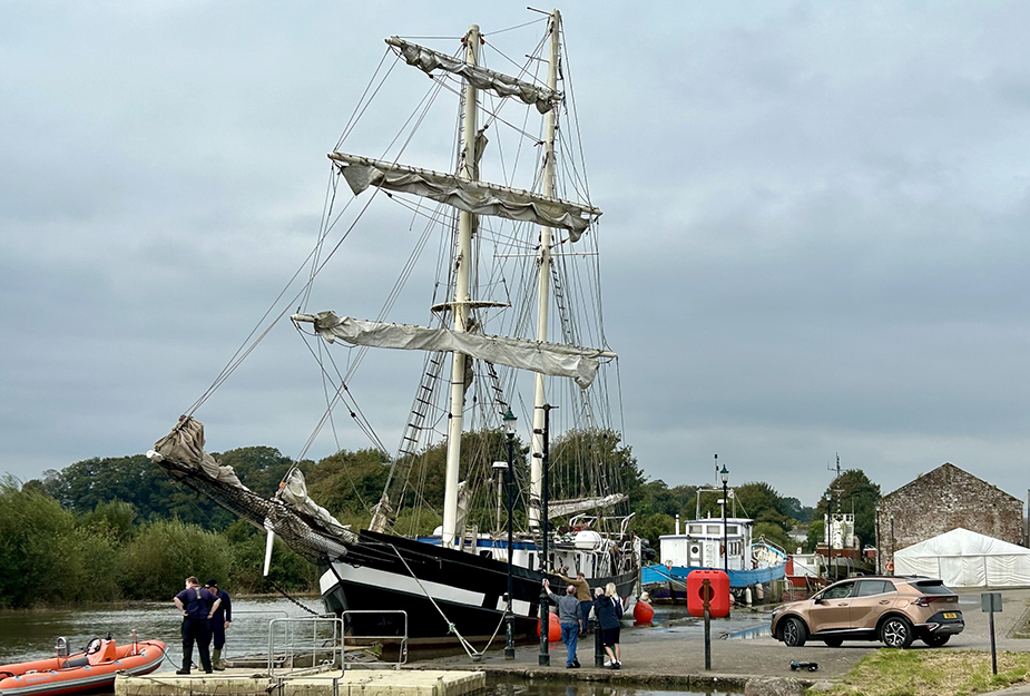 A ship docked at Annan Harbour with people walking around it.