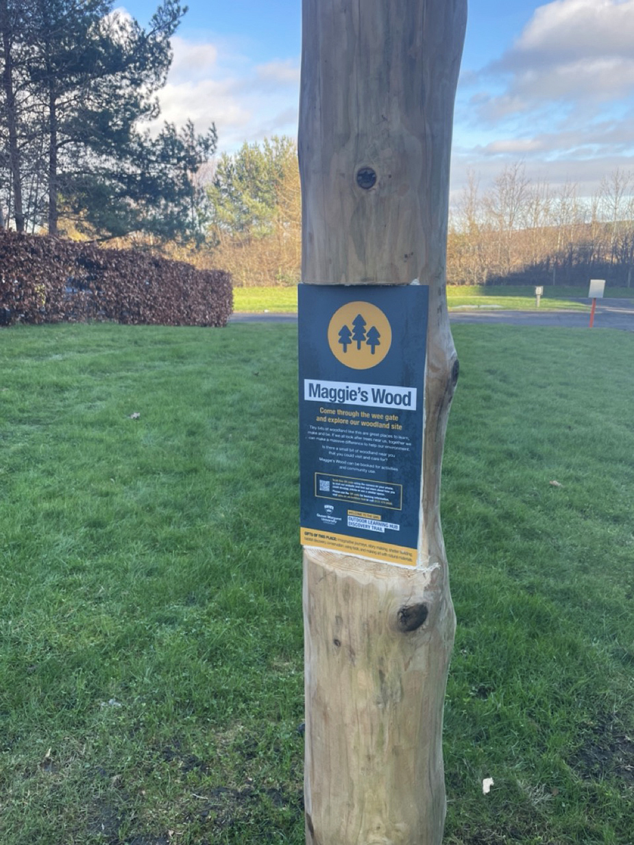 A wooden post sign with the words 'Maggie's Wood'.