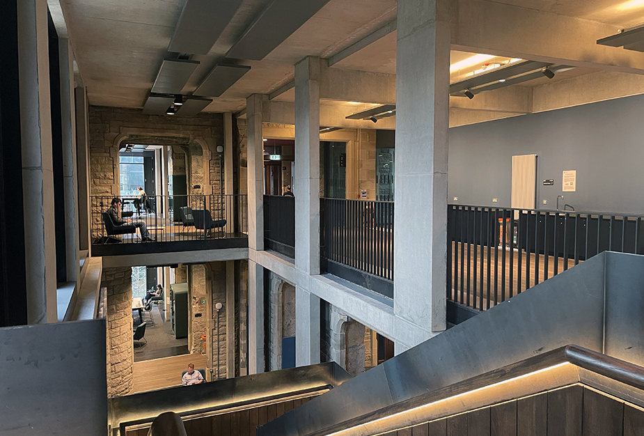 A multi-level modern interior featuring stone walls and open spaces, with people reading and working in a bright, inviting atmosphere.