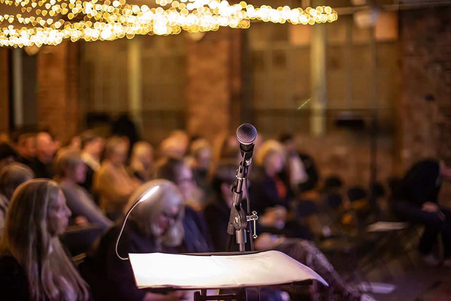 People sat down at an event in the background with a Mic stand in the foreground.