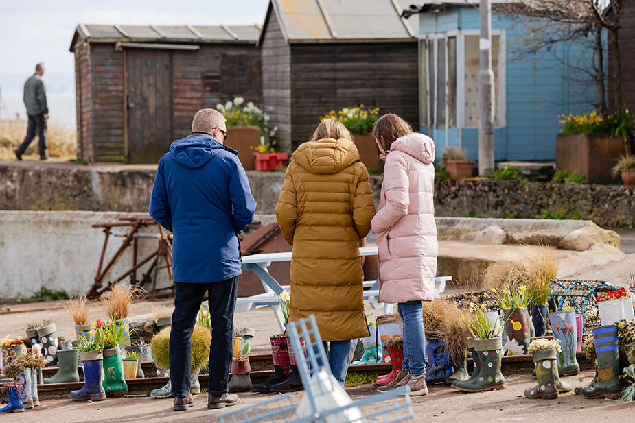 Three people pointing and looking at wellies used as planter at the seafront.