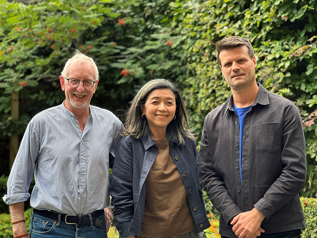 Three people smiling at the camera surrounded by a living wall (leaves and plants).