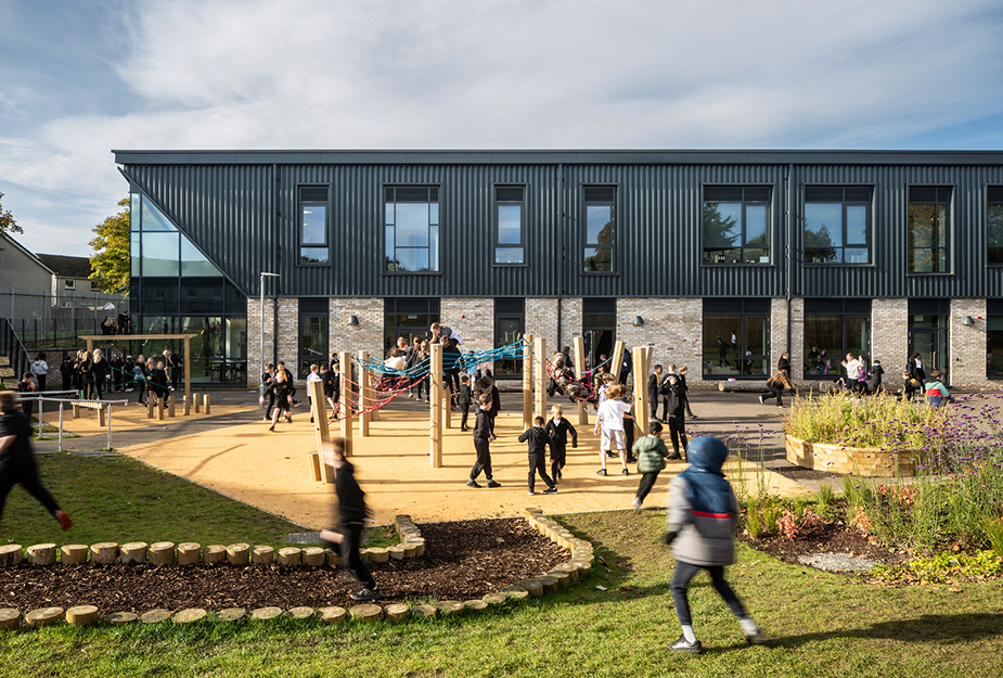 Children play in an outdoor school courtyard with climbing equipment, gardens, and a modern brick-and-metal school building.