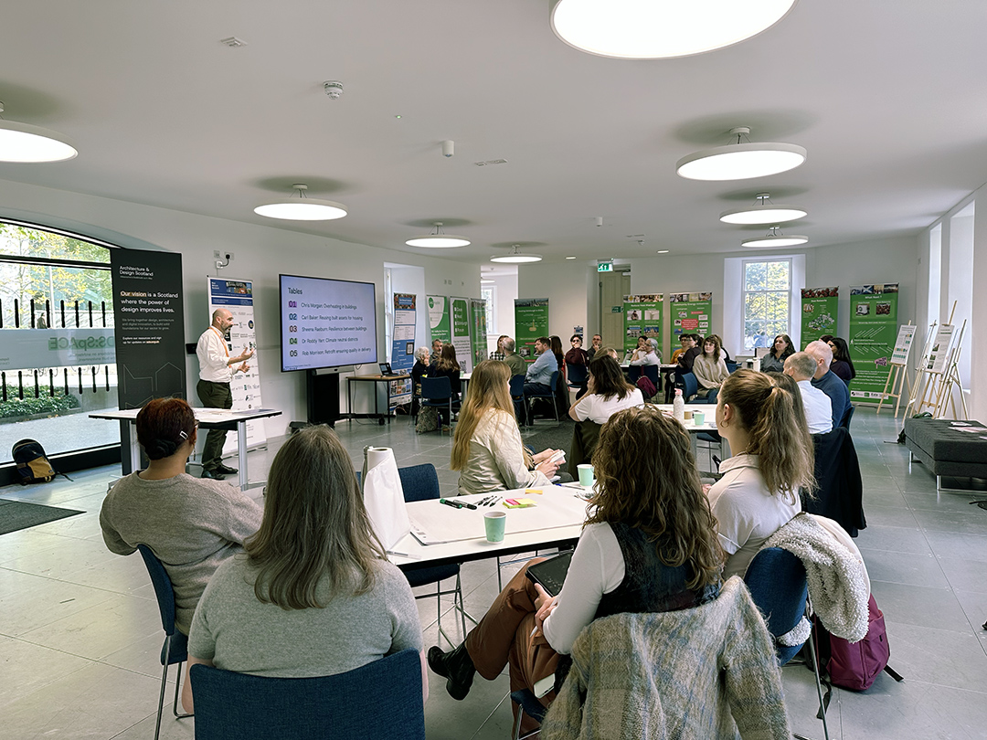 Groups of people sat around tables listening to Director of Design from Archicture and Design Scotland present at the Climate Clinic.